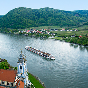 Photo of a ship cruising the river bank near Njord Durnstein with green hills in the background