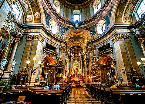 Interior of a Vienna Cathedral with mulitcolored murals, gold gilded columns, and an intricate design.