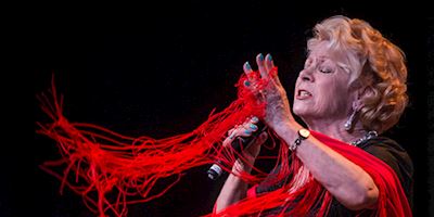 A woman with red fringe singing emotionally into a microphone.