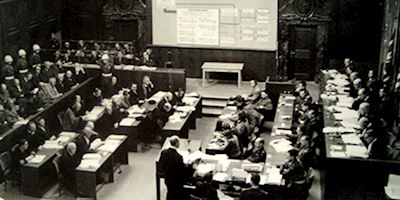 A black and white photo of a room full of desks and people at the Nuremberg Historic Trials.