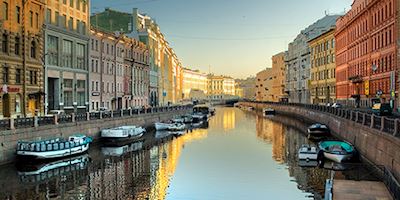 A canal in St. Petersburg, lined with boats and colorful houses, sparkles in dawn light.